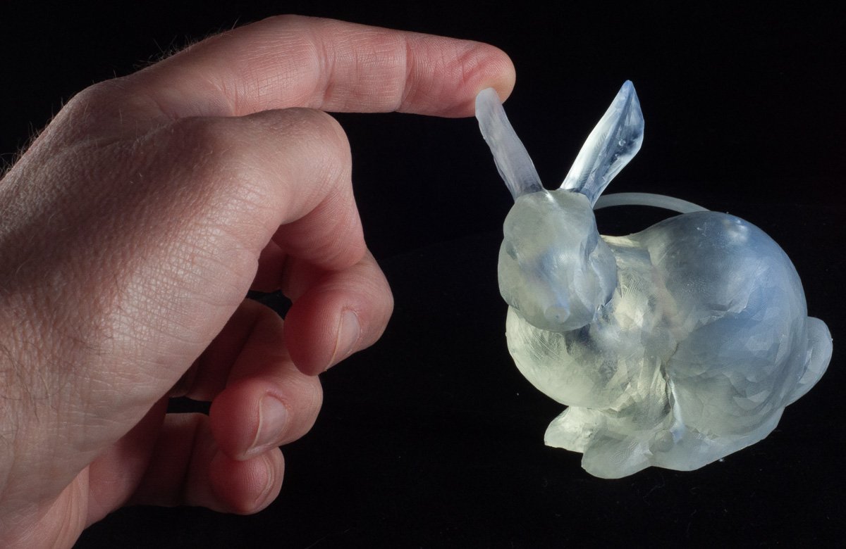 A translucent 3D-printed rabbit model with elongated ears is gently touched by
a person’s finger against a black background
