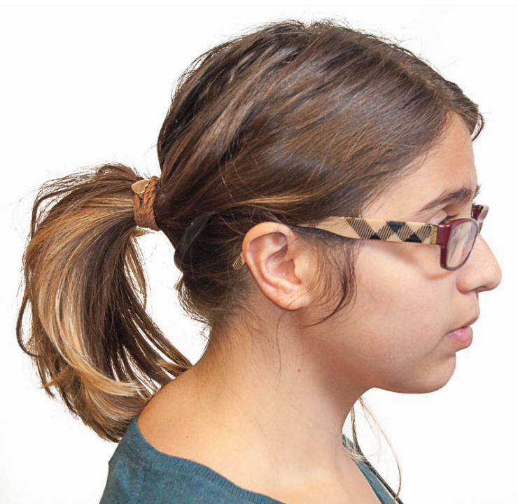 Profile view of a person with brown hair in a ponytail and wearing glasses
with a checkered pattern. They are wearing one of the before-mentioned
microphones, but it is hidden within their hair.