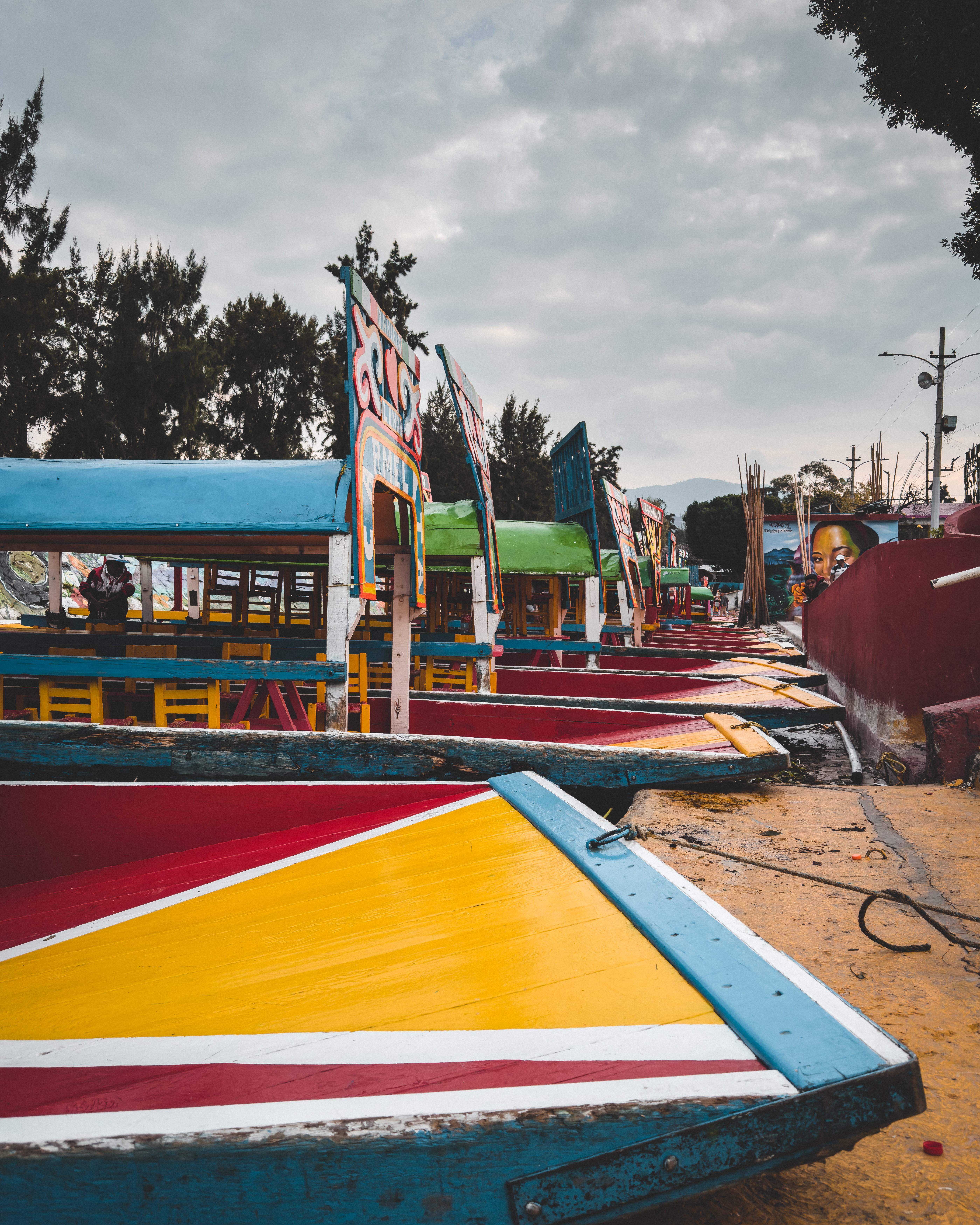 Colorful wooden boats with decorative signs are docked side by side under a
cloudy sky, capturing a lively scene at a canal or riverside
pier.
