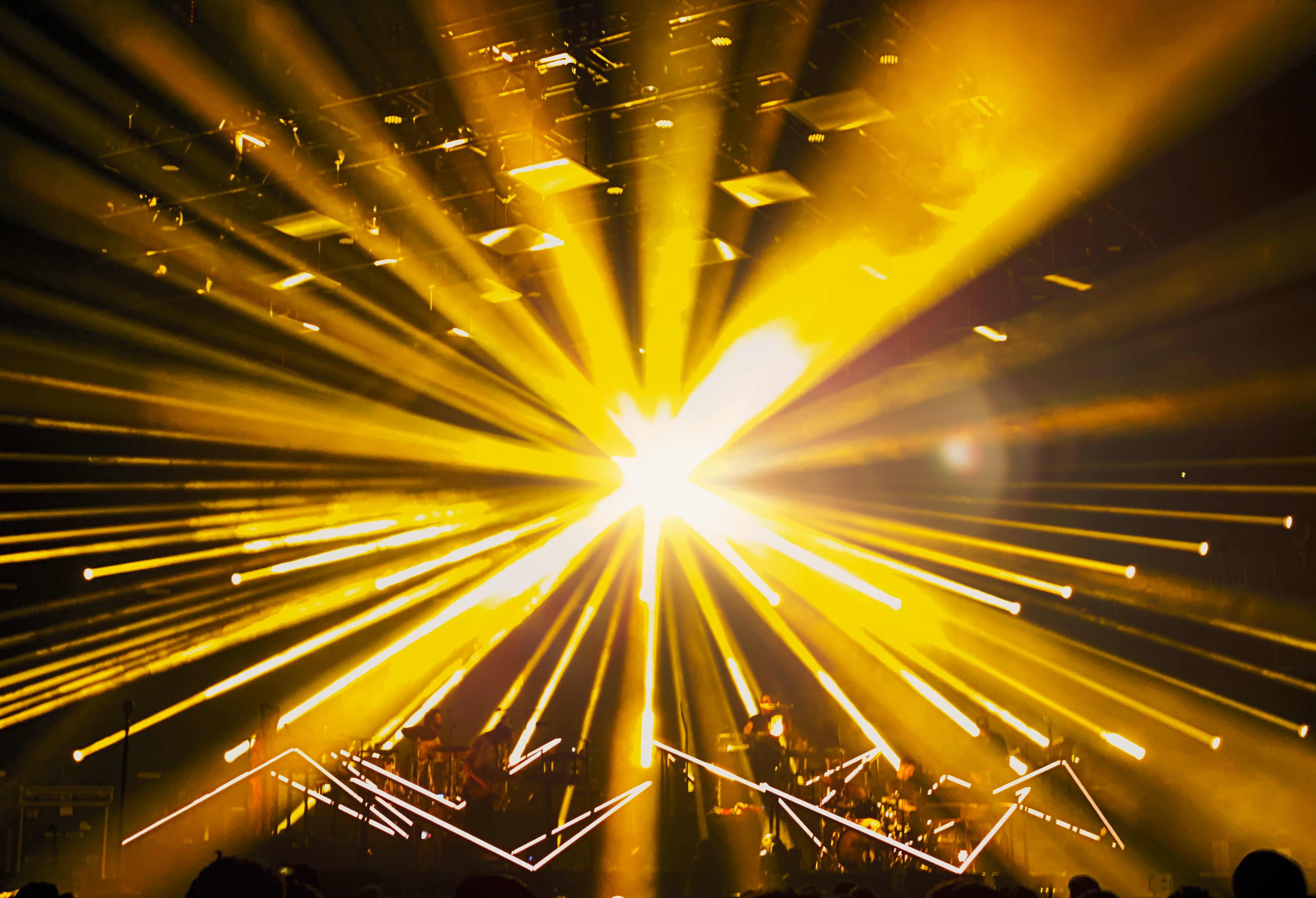 A stage concert with intense yellow spotlights radiating outwards, creating
dramatic beams of light over musicians performing
below.