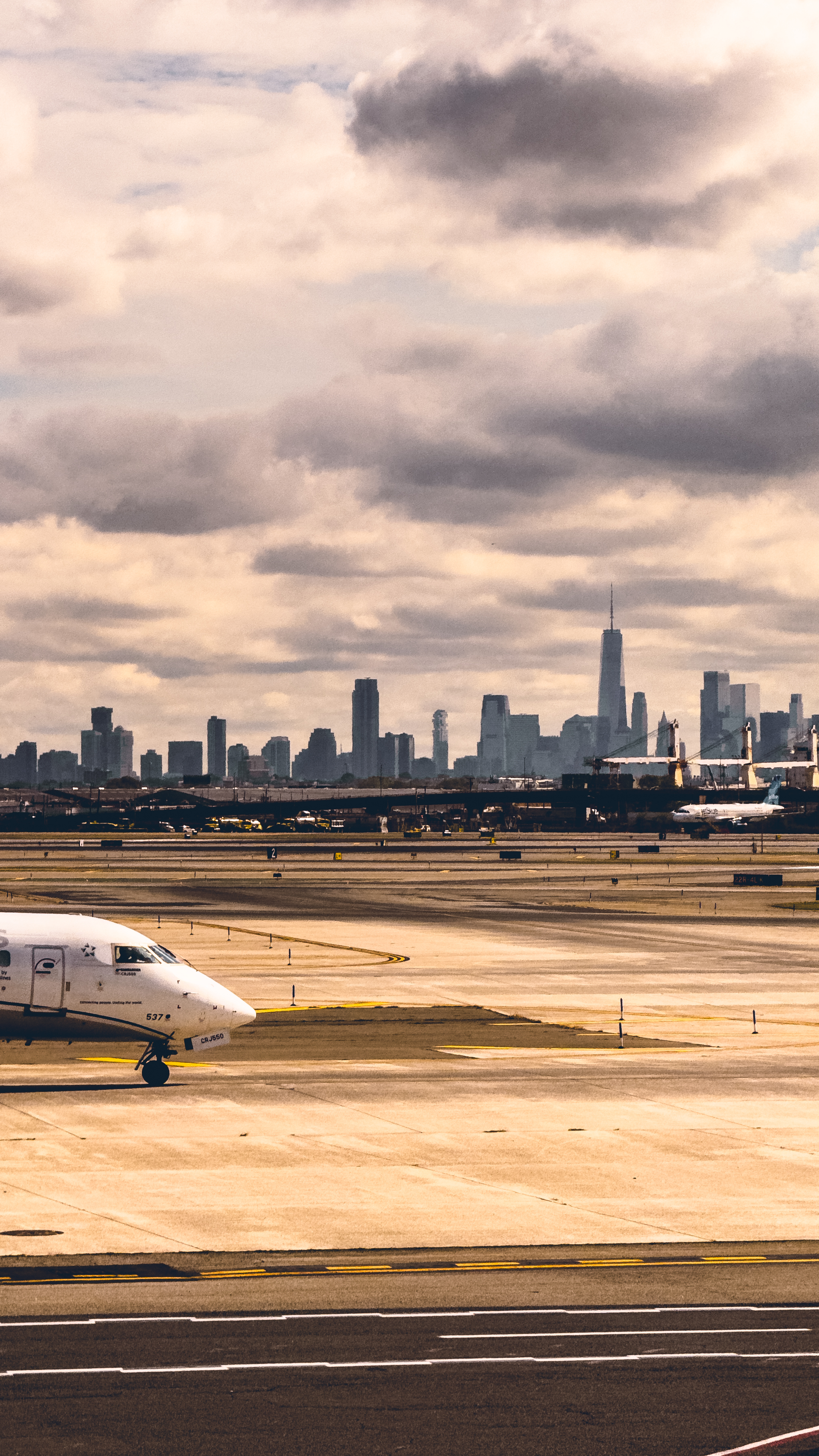 Commercial airplane taxiing on airport runway with dramatic city skyline and
cloudy sky in the background