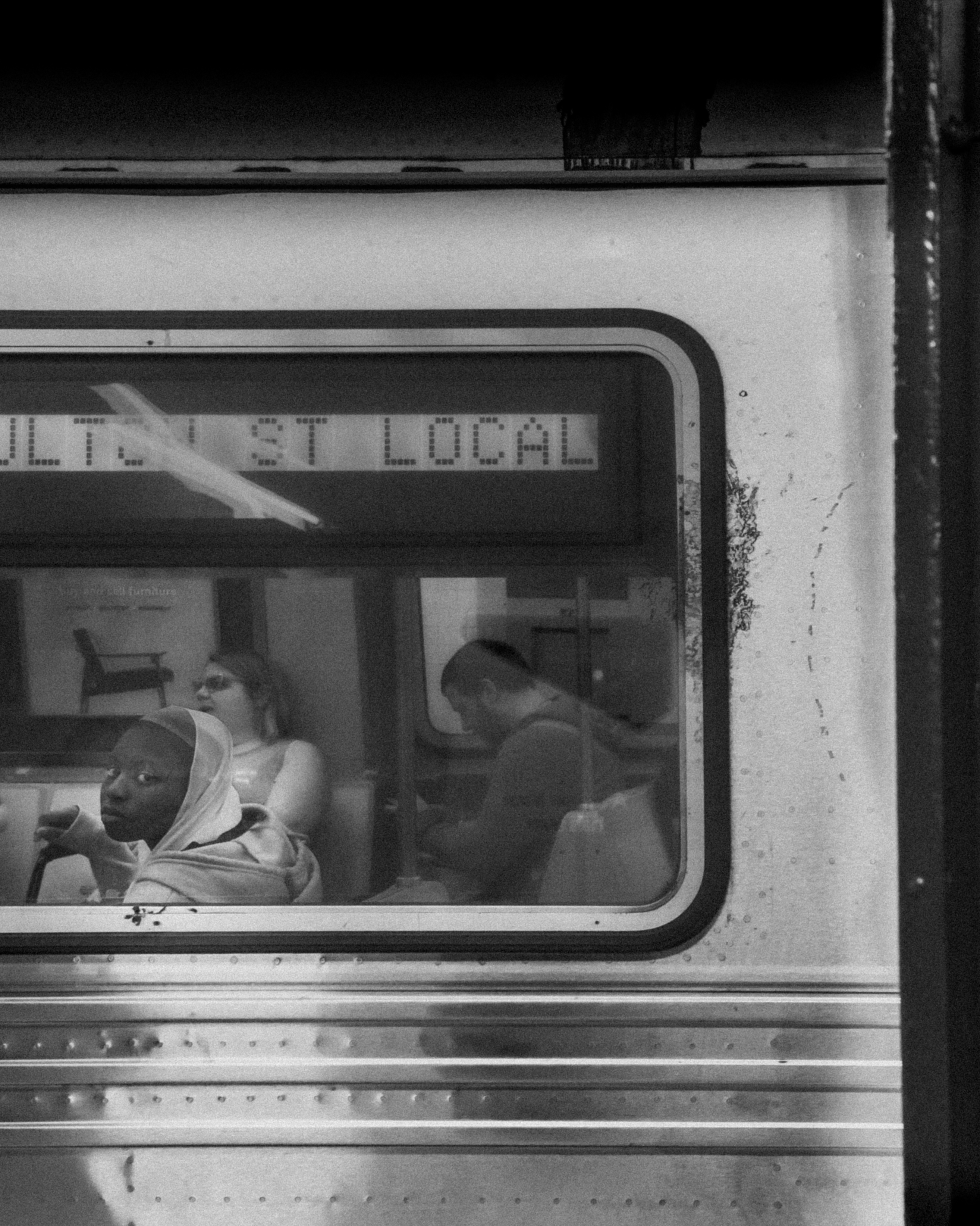 Passengers riding on a city subway, seen through a window with reflections and
signage