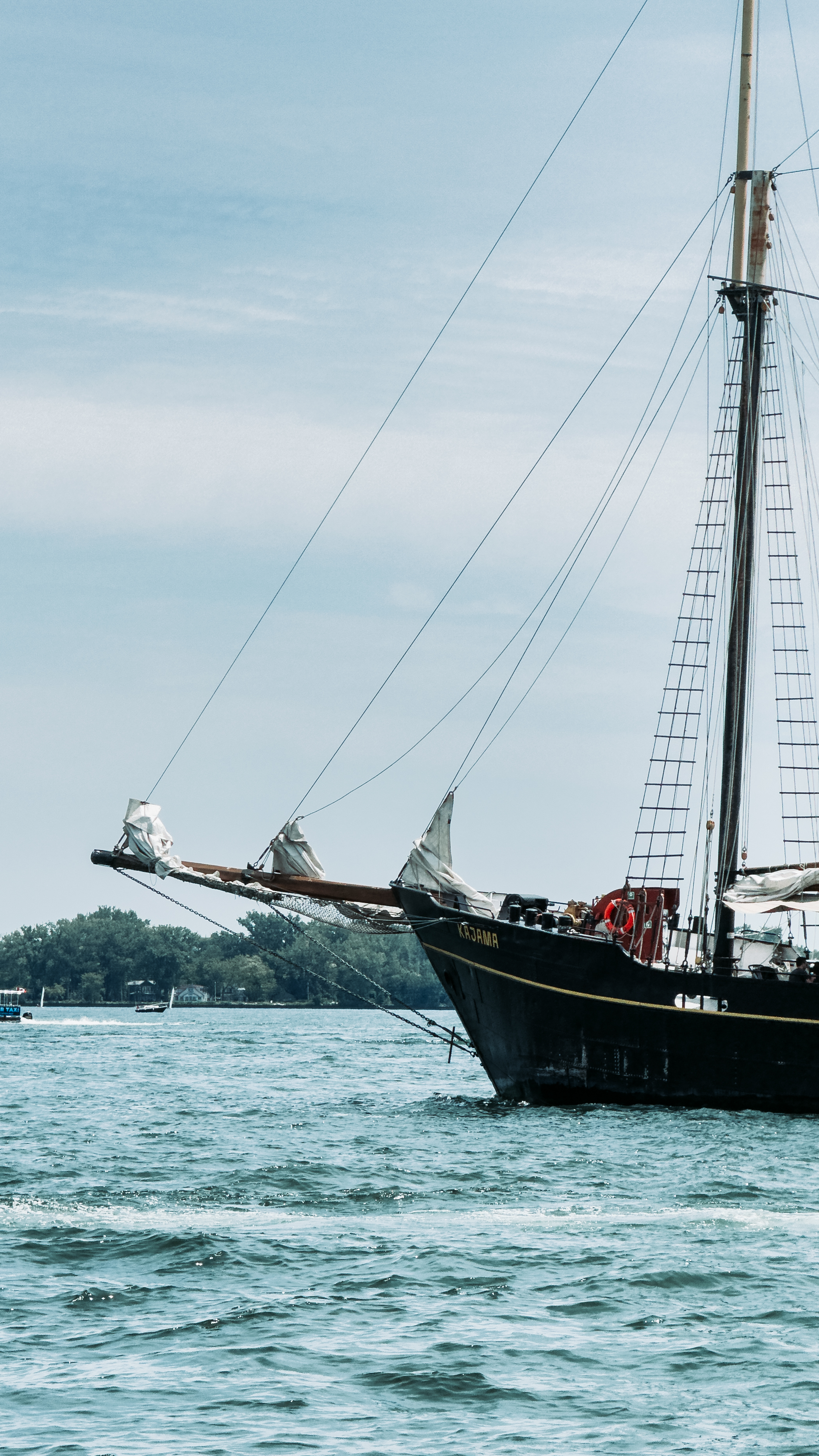 Tall-masted sailboat anchored in blue waters with distant shore and sky in the
background