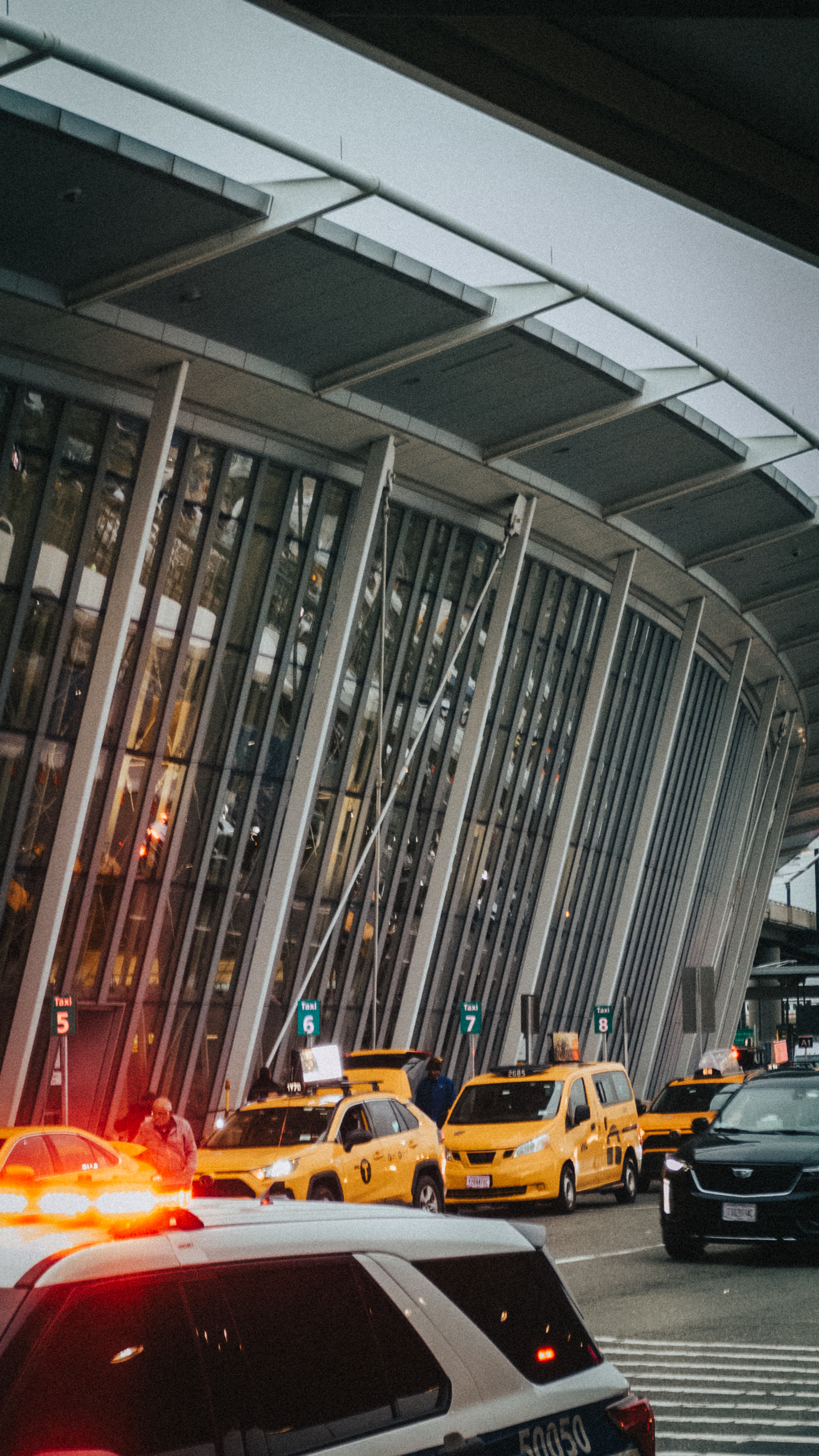 A line of yellow taxis and cars in front of the glass facade of a modern
airport terminal.