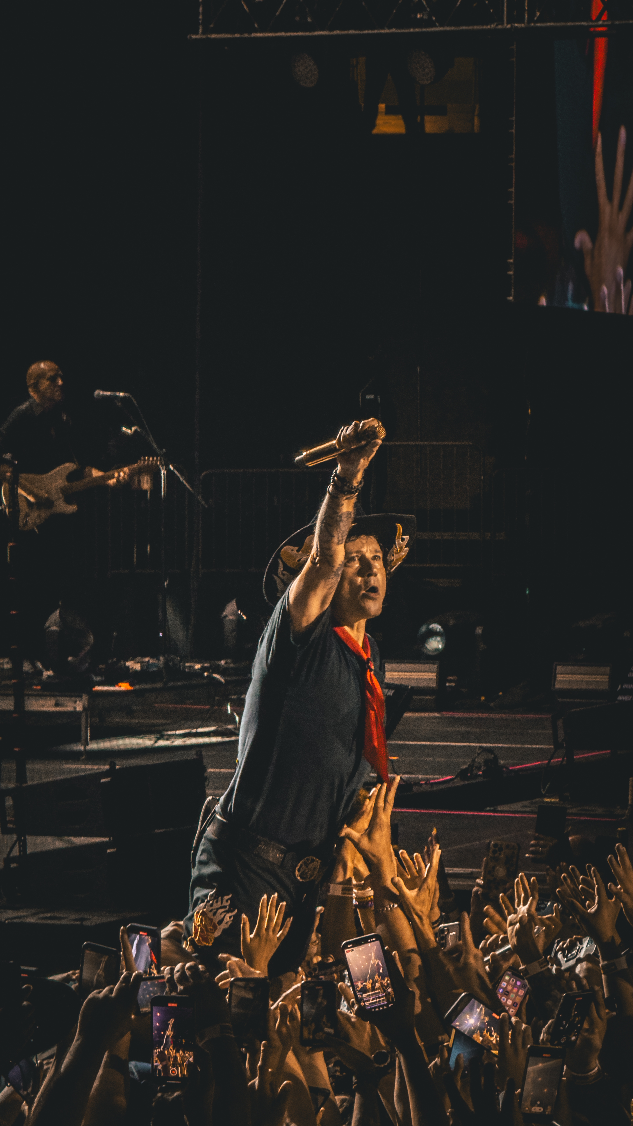A singer performing energetically on stage, reaching out to the audience while
fans capture the moment with their phones.