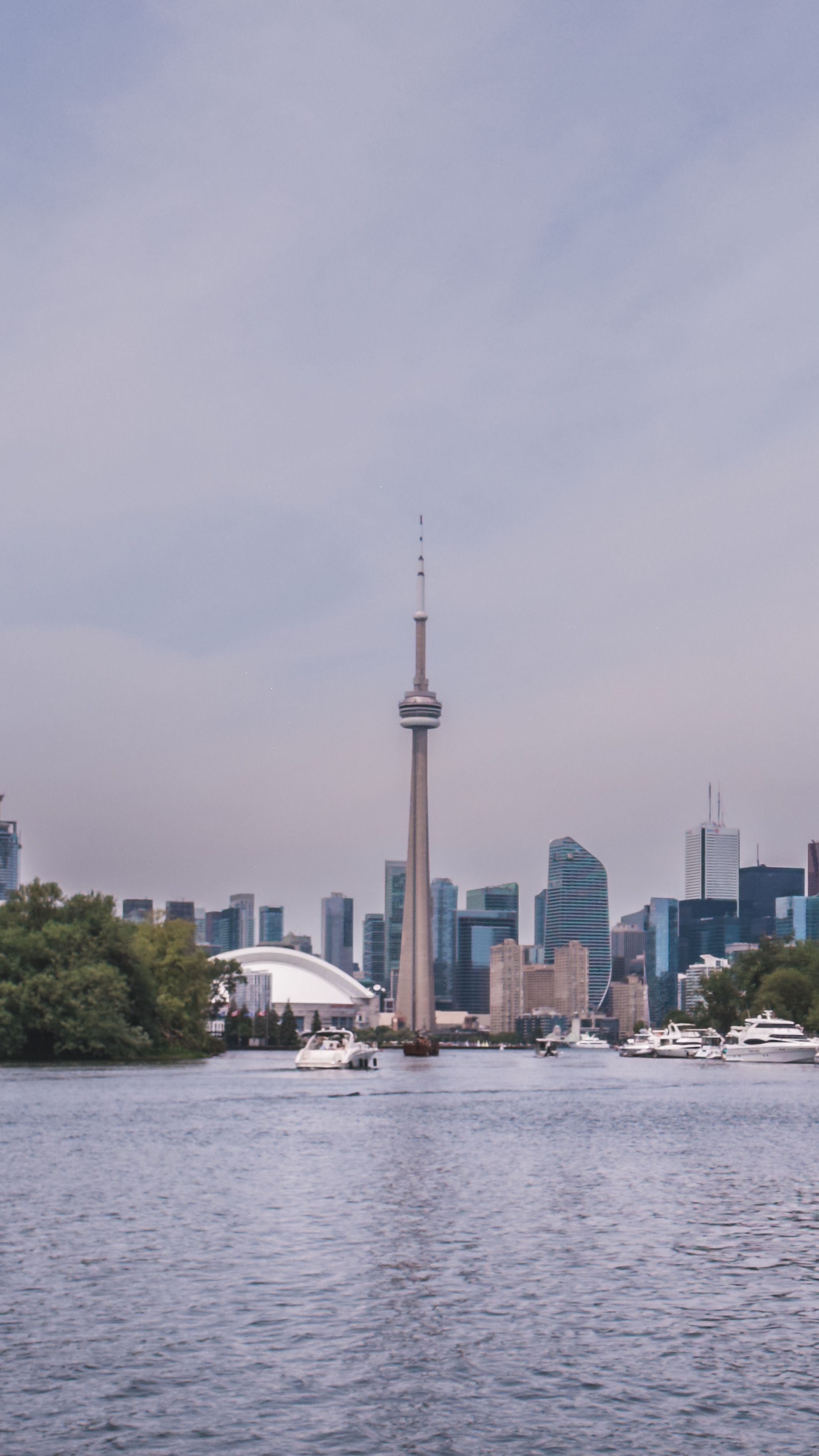 A city skyline view from the water with the CN Tower prominently in the
center, boats floating in the foreground, and modern skyscrapers lining the
horizon.