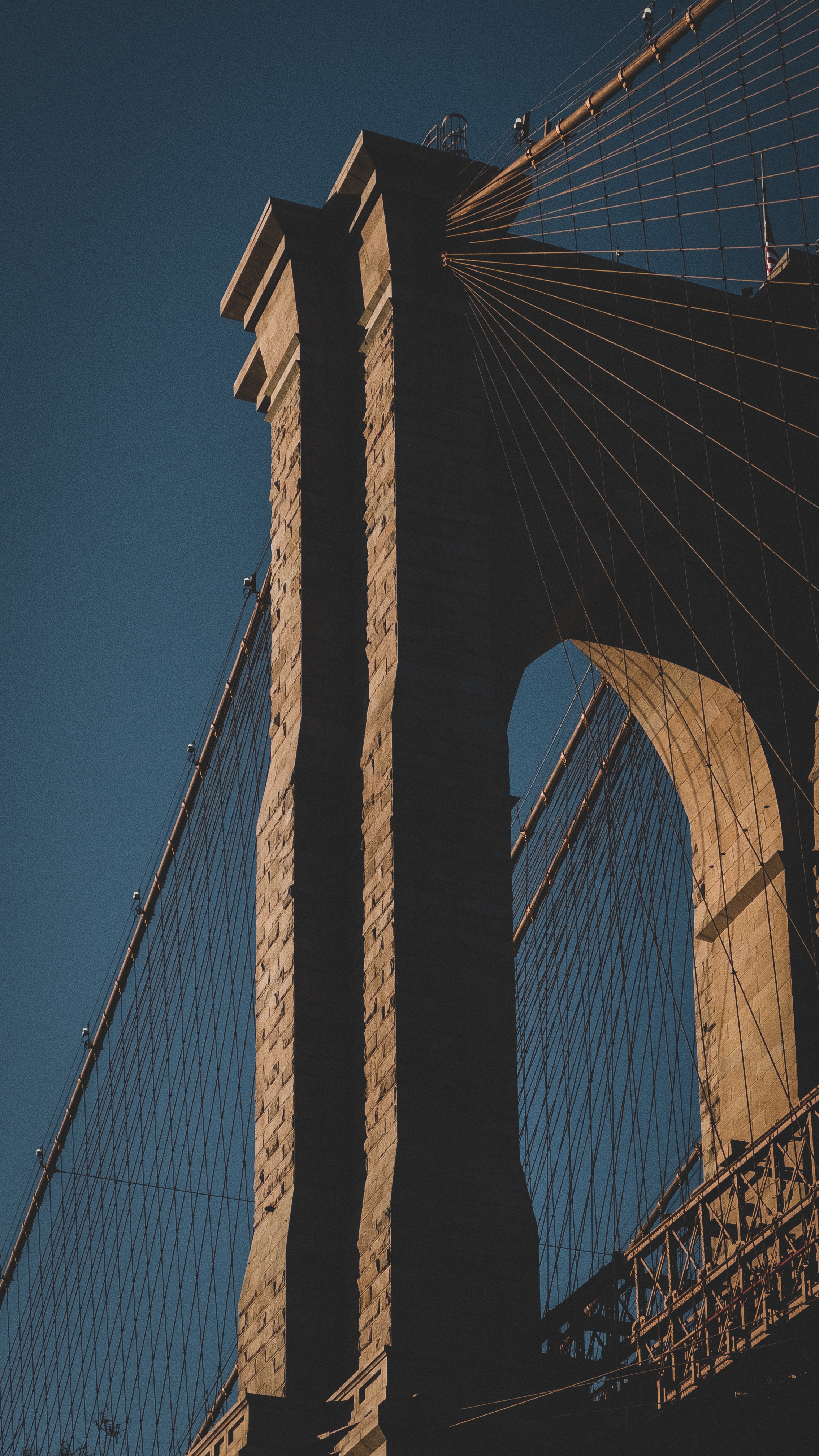 A close-up of the Brooklyn Bridge’s stone tower and suspension cables,
dramatically lit against a deep blue evening
sky.